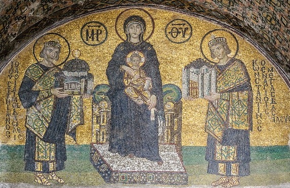 Southwestern entrance mosaic of Hagia Sophia. The Virgin Mary is standing in the middle, holding the Child Christ on her lap. On her right side stands emperor Justinian I, offering a model of the Hagia Sophia. On her left, emperor Constantine I, presenting a model of the city. Public domain.