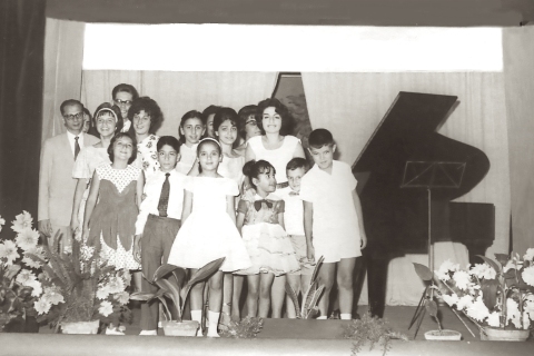 Μαθητική συναυλία του Εθνικού Ωδείου Αλεξανδρείας στην Αίθουσα «Αισχύλος-Αρίων» υπό την καθοδήγηση της καθηγήτριας Φιφίκας Μπρουσιανού. Διακρίνονται αριστερά ο καθηγητής πιάνου Σπύρος Κίζας και δεξιά ο μικρός Τάκης Πιζάνης. Αλεξάνδρεια 1962.